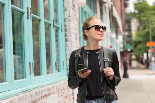Beautiful blond young female tourist using smart phone app guite on city break weekend trip to New York.