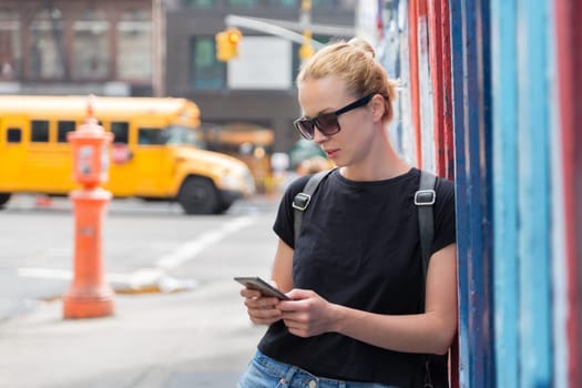 Closeup of female hipster with smart phone. Woman using smartphone against colorful graffiti wall in East Village, New York city, USA.