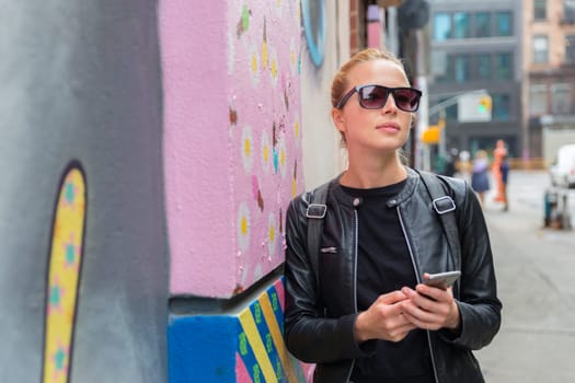 Closeup of female hipster with smart phone. Woman using smart phone app guite on city break weekend trip to East Village, New York city, USA.