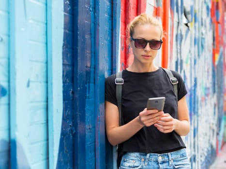 Closeup of female hipster with smart phone. Woman using smartphones against colorful graffiti wall in East Village, New York city, USA.