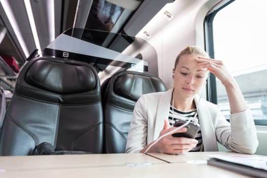 Businesswoman communicating on cellphone using headphone set while traveling by train in business class seat.