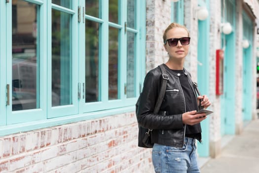 Beautiful blond young female tourist using smart phone app guite on city break weekend trip to New York.