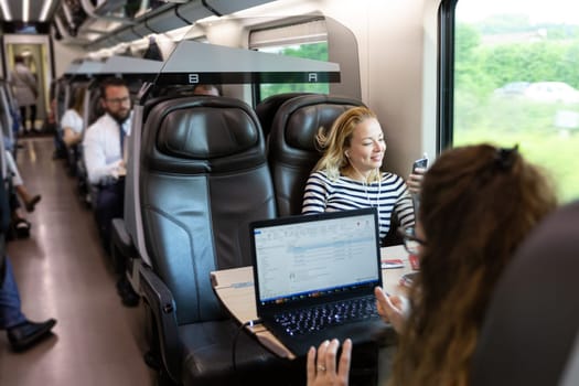 Businesswoman communicating on cellphone using headphone set while traveling by train in business class seat.