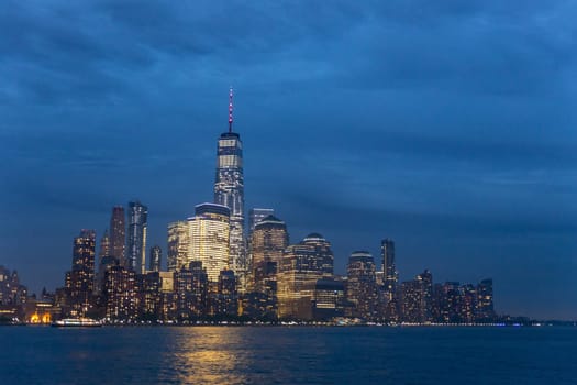 Panoramic view of Lower Manhattan from Ellis Island at cloudy dusk, New York City.