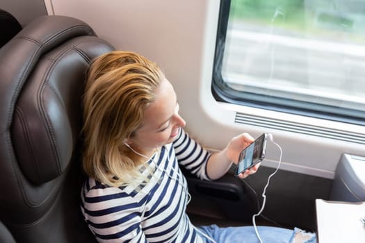 Woman communicating on cellphone using headphone set while traveling by train in business class seat.