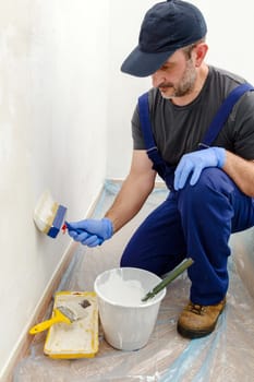 Painter paints the wall with the tint of white. Wall with serious moisture problems. Detail of the brush. white dye is prepared for the painter's job.