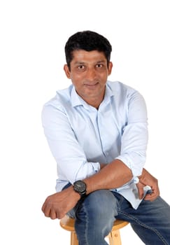 A handsome good looking East Indian man sitting on a chair and relaxing.looking into the camera, isolated for white background.