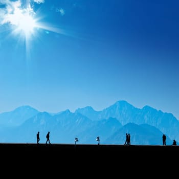 Silhouetted people relaxing on street over blue sky and high mountains