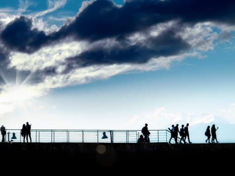 silhouetted people walking over sunny and cloudy blue sky