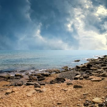 seascape image of sandy and rocky beach over stormy sky