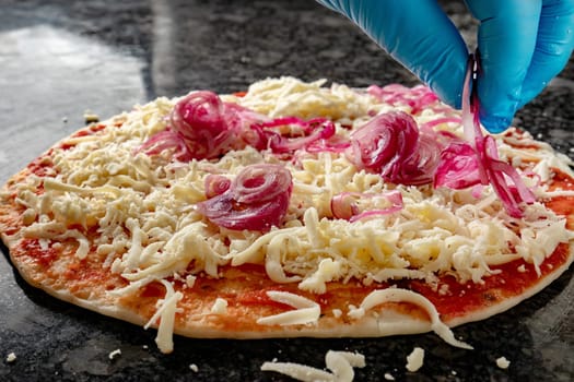 Hand with glove spread onion over the cheese pizza