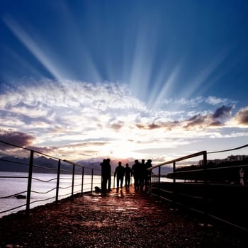 silhouetted people walking on street over sunset sky with sunbeam