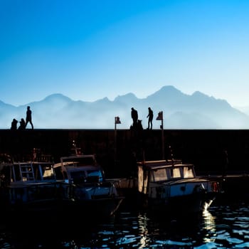 silhouetted people walking in harbor of Antalya over sunny sky