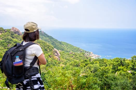 Women tourist with a backpack wear cap standing look at beautiful nature landscape blue sea under the summer sky from high scenic viewpoint at Koh Tao in Surat Thani, Thailand