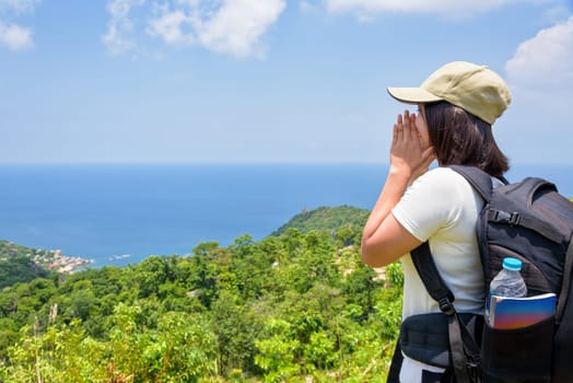 Women tourist with a backpack wear cap raise hand at the mouth yelling and beautiful nature landscape blue sea and sky from high scenic viewpoint at Koh Tao, Surat Thani, Thailand
