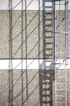 A fire escape on the side of an apartment building casts a shadow.