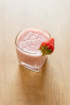 Fresh strawberry smoothie cold drink. Milkshake in glass on wooden table. Fruits for decoration