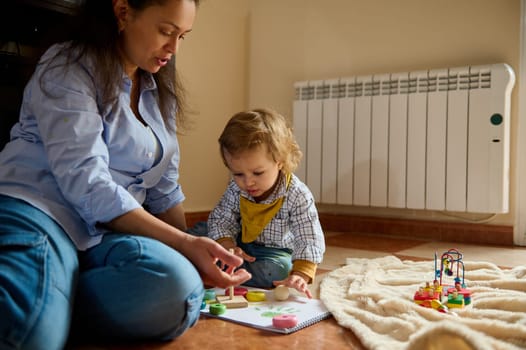 A mother plays and teaches her toddler child at home on wooden floor, fostering joy and connection.