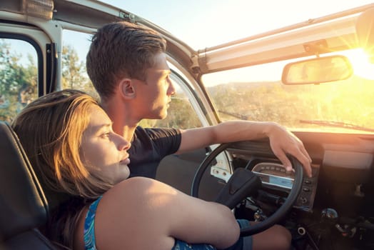 Happy young couple in a car enjoying the beautiful sunset in countryside.