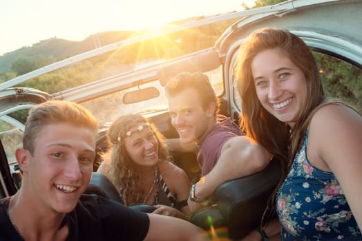 Group of happy people in a car at sunset in summer.