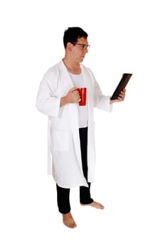 A handsome tall man standing in a white bathrobe and his tablet and.a red coffee mug bare feet isolated for white background.
