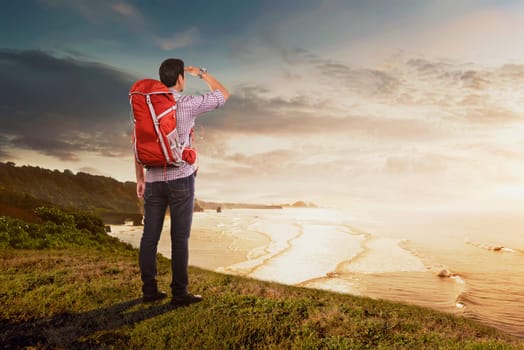 Rear view of asian traveler man with backpack looking at panorama from cliff