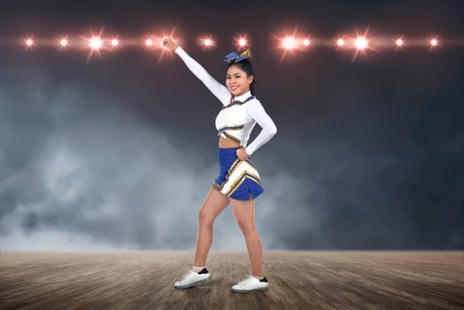 Attractive asian cheerleader in action with spotlights on background