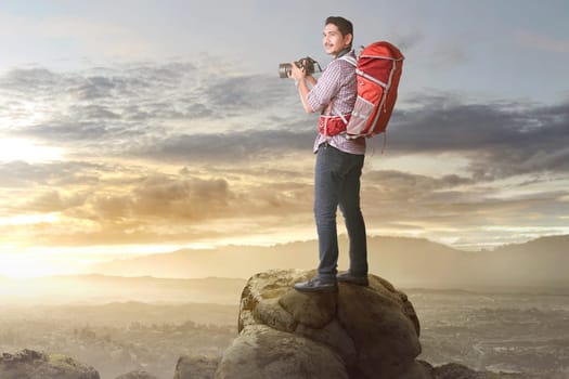 Happy asian tourist with camera and backpack ready to take a photo on the mountain