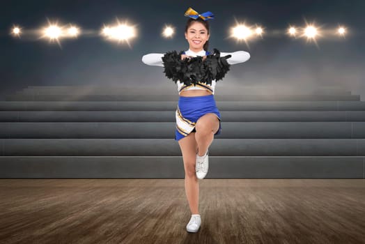Smiling asian cheerleader in action with pom poms at indoor