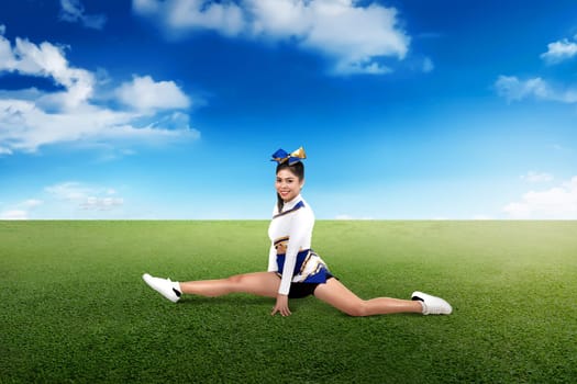 Beautiful asian cheerleader doing splits on green field