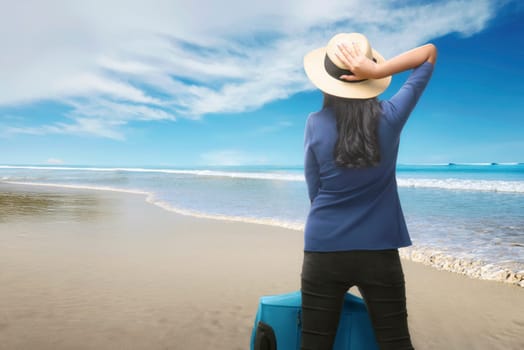 Rear view of asian traveler woman with suitcase relaxing on the beach