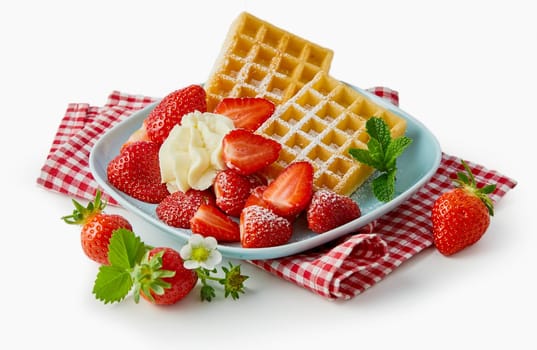 Fresh ripe strawberries with waffles and cream served on a rustic checkered red and white napkin over a white background
