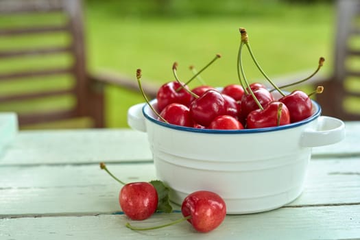 Close-up of a bowl full of sweet fresh cherries on a rustic wooden table outdoors in the garden