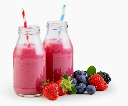 Fresh liquidised berry smoothies in glass bottles with strawberries, blueberries and blackberries alongside isolated on white with copy space