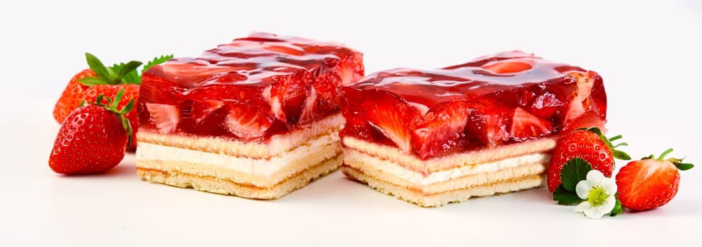 Two slices of strawberry and cream layer cake or tart topped with fresh ripe fruit in a syrup in a panorama banner on white