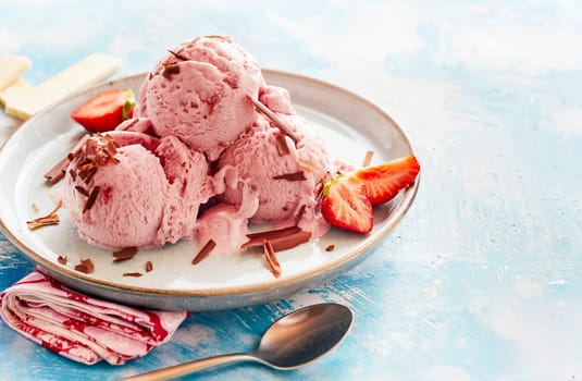 Tasty strawberry ice-cream sundae in a parlour topped with flakes of chocolate and fresh berries over a mottled blue background with copy space