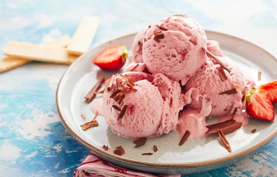 Sundae with three scoops of craft ice cream flavored with fresh strawberries and garnished with chocolate shavings served on a pottery plate