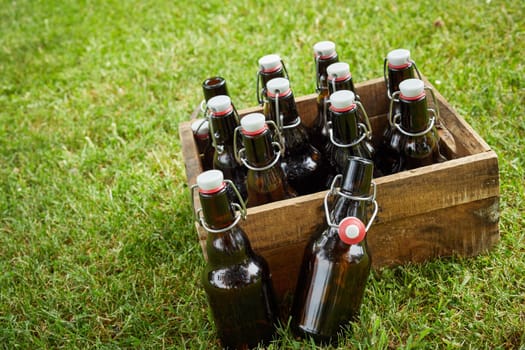 Wooden crate with unlabelled bottles of beer or lager at a tilted angle outdoors on green grass with copy space for a summer picnic