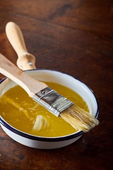 Small saucepan of melted butter for baking with a basting brush for glazing the pastries on a wooden kitchen table with copy space
