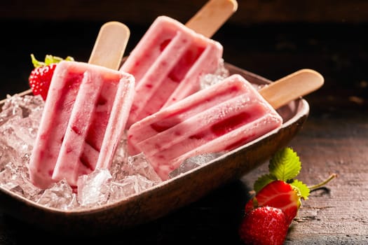 Tasty ice lolly with strawberries on a plate filled with crushed ice.