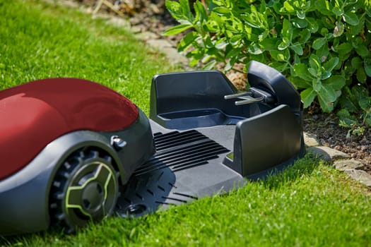 Close-up of a red autonomous mower moving towards the charging station in the garden