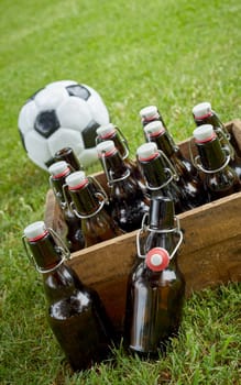 Bottled beer in an old wooden crate with a championship soccer ball on green grass ready for a party celebration and get together for the World Cup in a tilted angle close up view