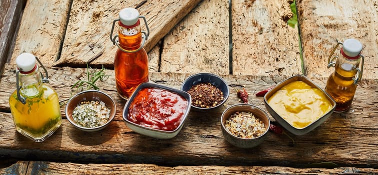 Assorted sauces, dips, spices and aromatic oils for preparing a barbecue arranged ready for cooking on an old rustic vintage wooden table viewed high angle in panorama format