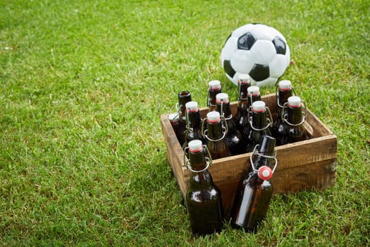Old wooden crate of bottled craft beer with a soccer ball on fresh green grass with copy space conceptual of the World Cup