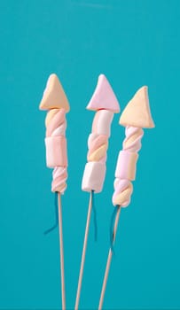 Three unique creative marshmallow edible fireworks in the shape of rockets for a party or holiday celebration on a turquoise blue background with copyspace