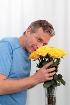 Mature male holds a dozen yellow pink roses happy. Man smilies smelling a bunch of aromatic roses. Middle-aged man holds a yellow pink roses bouquet, thankful for the aroma smiling at the viewer.