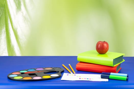 Colorful school equipment and two books on dark blue table against light green background. Space for your text or dsiplay product montage.