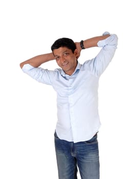 A happy smiling Asian man standing in jeans and a light blue shirt with.his hands behind his head, isolated for white background.