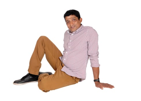 A tall middle age East Indian man sitting in brown pants and red checkered.shirt on the floor, isolated for white background.