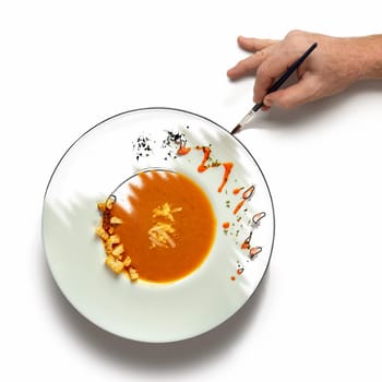 Hand painting over a plate of creamy vegetable soup. Concept for a cooking at the level of art.